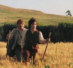 two young men walking through a field with stick and spear in their hands, one holding the other's arm