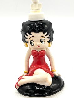 a ceramic figurine sitting on top of a black base and wearing a red dress