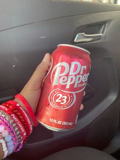 a person holding up a can of dr pepper soda in their car's dashboard