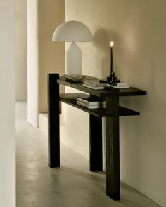 a table with a lamp on it next to a white wall and a book shelf