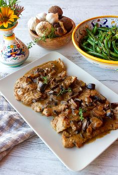 a white plate topped with meat covered in mushrooms next to green beans and other vegetables