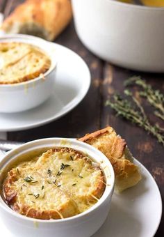 two white bowls filled with soup on top of a wooden table next to some bread