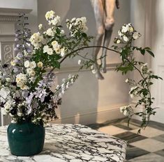 a vase filled with white and purple flowers on top of a marble table next to a statue