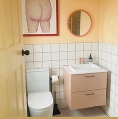 a white toilet sitting next to a sink in a bathroom under a painting on the wall