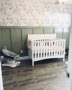 a white crib in a room with floral wallpaper on the walls and wooden flooring