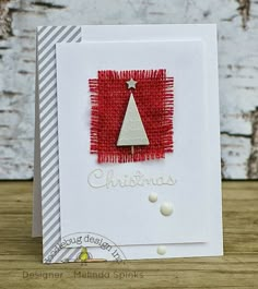 a christmas card with a red and white tree on it's front, sitting on a wooden table