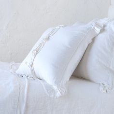 two white pillows sitting on top of a bed next to each other with ruffled edges