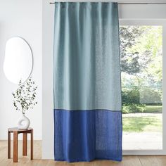 a blue curtain hanging in front of a window next to a wooden table and mirror