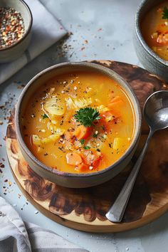 two bowls filled with soup on top of a wooden plate next to silver spoons