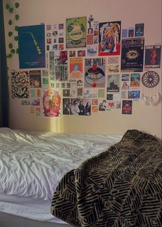 a bed with white sheets and lots of posters on the wall next to it's headboard