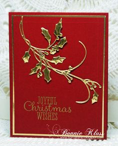 a red christmas card with gold foiling and holly leaves on it, sitting on a white background