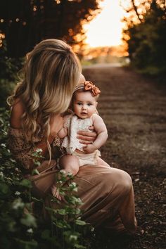 a woman holding a baby in her arms while the sun is setting on the horizon