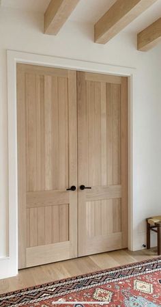 two wooden doors in a room with a rug on the floor and a table next to it