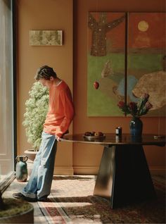 a woman standing in front of a table with a vase on it next to a potted plant