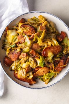 a white bowl filled with sausage, cabbage and other food on top of a table