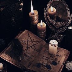 an open book sitting on top of a table next to candles and other items in front of a mirror