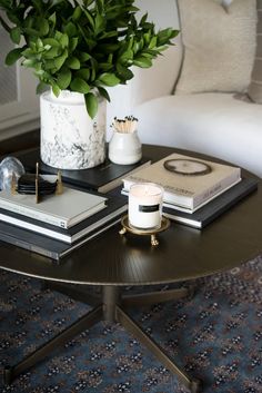 a coffee table topped with books and a vase filled with green plant sitting on top of it