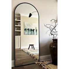 an arched mirror in the corner of a room next to a table and vase with a painting on it