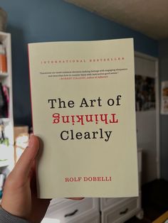 a person holding up a book about the art of surpuul clearly by roup dobelli