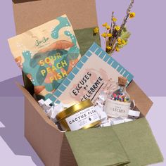 an open box filled with lots of different types of items and flowers on top of a purple background