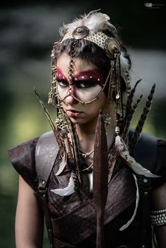 a woman with feathers on her head and makeup is posing for the camera, wearing an elaborate costume