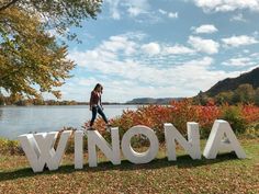 a woman standing on the word winona in front of a body of water and trees