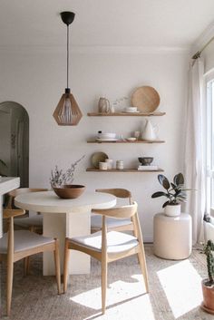 a dining room table with chairs and shelves on the wall above it, next to a potted plant