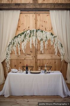 the table is set with wine bottles and flowers in front of an open barn door