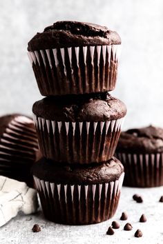 three chocolate muffins stacked on top of each other with chocolate chips scattered around them