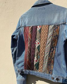 a denim jacket with different colored ties on it hanging up against a white building wall