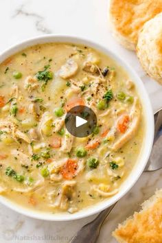 a bowl of chicken pot pie soup on a marble table with two rolls and a spoon