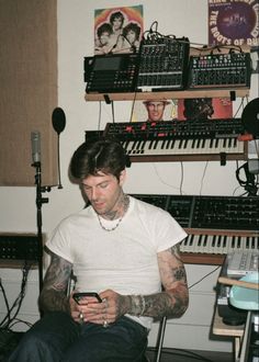 a man with tattoos sitting in front of a keyboard and looking at his cell phone