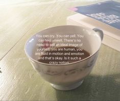 a coffee cup sitting on top of a wooden table with a book in the background