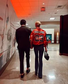 two people are walking down the hall in an office building, one is wearing a red jacket