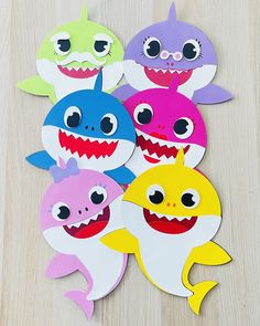 paper cutouts of different colors and sizes of sharks on a wooden table with white background