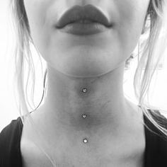 a woman wearing a necklace with three small dots on the bottom of her neck,