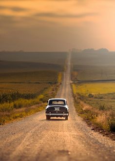 an old car is parked on the side of a dirt road in the middle of nowhere