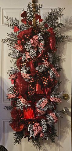 a red and black christmas wreath hanging on the front door with ribbons, bows and decorations