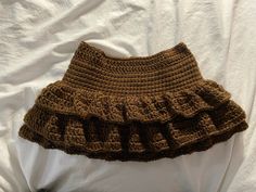 a brown crocheted skirt with ruffles on the bottom is laying on a white sheet