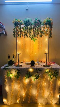 a table with lights and greenery on it in front of a wall hanging from the ceiling