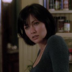 a close up of a person in a room with bookshelves and shelves behind her