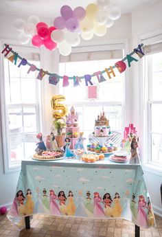 a princess themed birthday party with balloons, cake and desserts on a table in front of a window