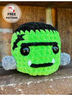 a crocheted green monster with black eyes and horns on it's head