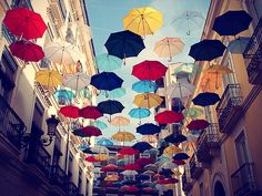 many colorful umbrellas hanging from the ceiling in an alleyway with buildings and balconies