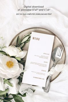 a table setting with white flowers, silverware and a menu card on a plate