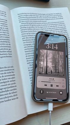 an open book with headphones attached to it next to a cell phone and ear buds