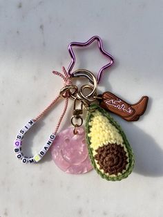 three crocheted keychains with charms attached to them on a white surface