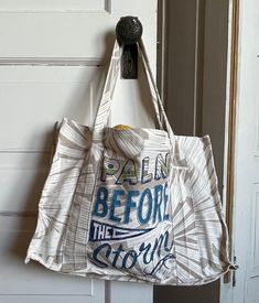 a white bag hanging on the door with words written in blue and grey letters that read calm before the storm