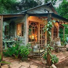 a small wooden cabin in the woods with lots of greenery on the front porch