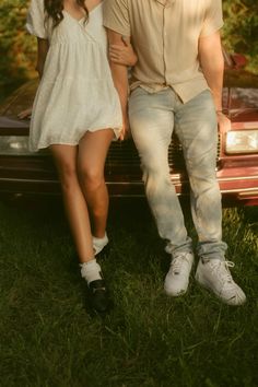 a man and woman sitting on the hood of a car in front of a tree